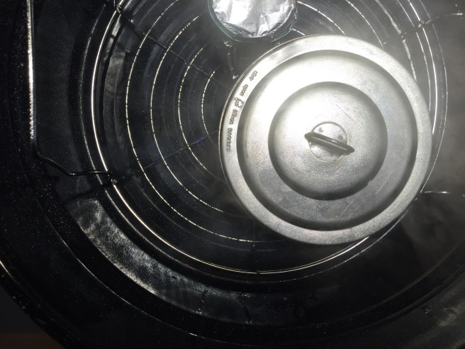 Plum pudding molds on top of a rack set in boiling water.